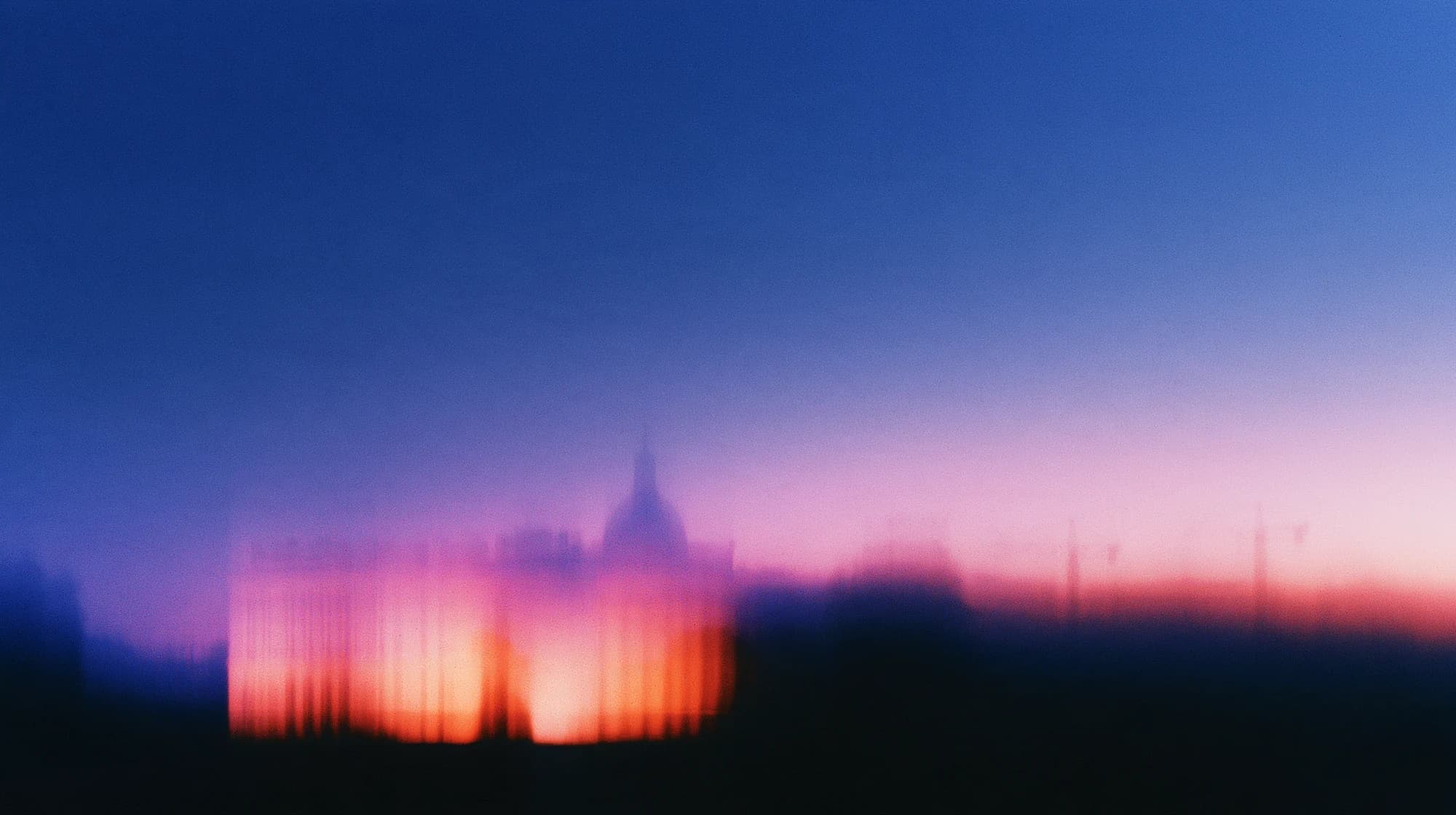 Unscharfe Silhouette eines herrschaftlichen Gebäudes vor einem blaurosa Morgenhimmel, rechts schemenhafte Baukräne.