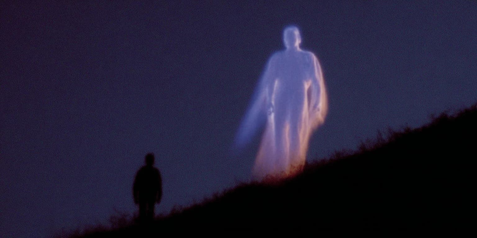 Eine kleine dunkle Gestalt steht in der Dämmerung an einem Hang unter einer riesigen, durchscheinend leuchtenden Gestalt in langem Gewand.