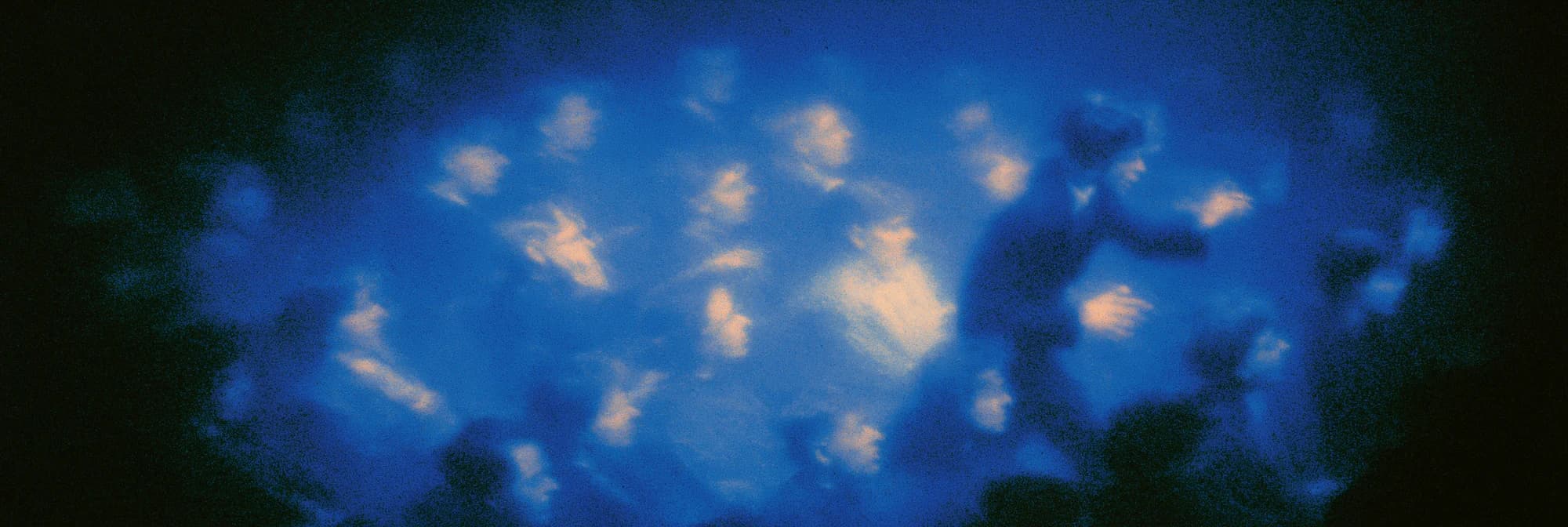 Eine verschwommene Menge von Gesichtern in tiefblauem Licht, von unten warm angestrahlt, rechts eine Gestalt in Bewegung.