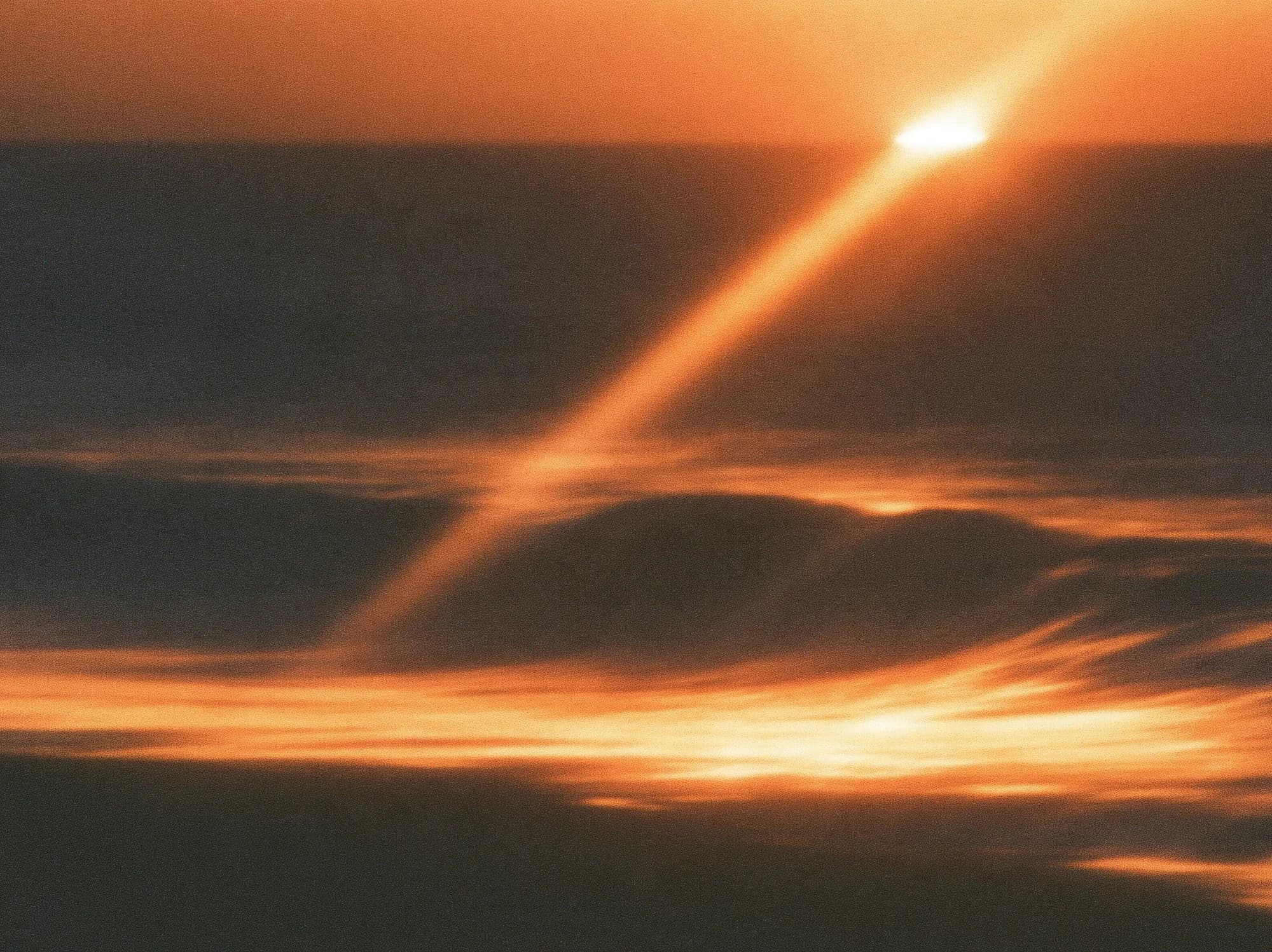 Bernsteinfarbenes Sonnenlicht über einer dunklen Küste und verschwommenen Wellen.